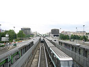 Croisement de rames de métro, bordés par une autoroute dans un environnement urbain.