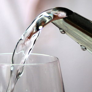 Air jernih tuang daripada muncung ke dalam gelas minum.