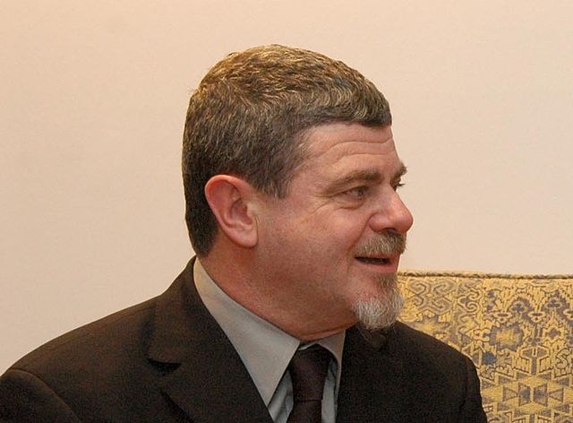 A man looking in profile with a gray suit, gray shirt and tie.