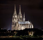 Голяма, ярко осветена катедрала седи в средата на хоризонта през нощта.