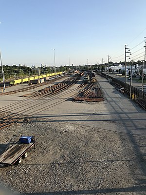 A rail yard is seen from a bridge. A group of tracks contain various rail maintenance equipment, such as a catenary maintenance vehicle and a train of hoppers loaded with track ballast.