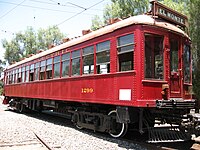 A 1930s streetcar, bright red, showing its front and right side