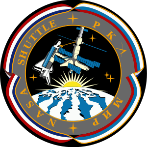 An illustration showing a space shuttle docked to a space station above a stylized version of the Earth. The Sun is rising over the Earth, and the image is surrounded by ribbon in red, white and blue. The words NASA, Shuttle, РКА and Мир are written around the image.
