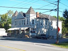 A large gray wooden building at the corner of a road with two pointy towers on either side and a less pointy roof between them. "IOOF Hall" is written below the central point