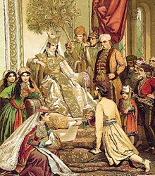 La reine Tamar, assise sur un trône haut, entourée de courtisans et sous un éventail de plumes de paon, regarde le poète Roustavéli à genoux devant elle alors qu'il lui tend un manuscrit.
