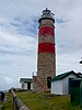 A light brown sandstone lighthouse with two red horizontal bands and red cupola