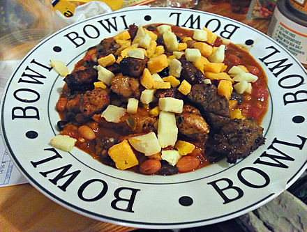 Bowl containing Chili con carne served in a Tex-Mex style, with pork, beef, cheddar and monterey jack on top.