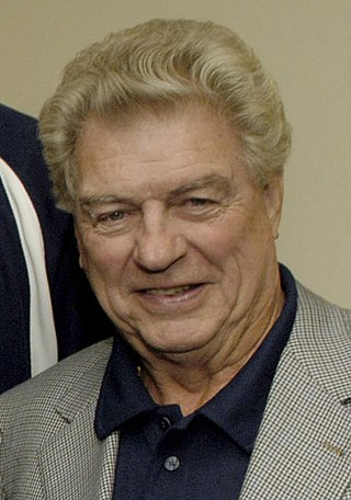 Headshot of a man smiling. He is wearing a checked coat with a blue shirt underneath.