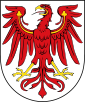 Argent an eagle Gules armed and beaked Or, langued Gules, the wings charged with a trefoil Or – i.e.: a red eagle with golden talons and beak and a red tongue, on a white background; the wings are overlaid with golden trefoils