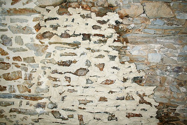 A stone wall in France with lime mortar grouting being applied. Right: unapplied. Centre: lime mortar applied with a trowel. Left: lime mortar applied