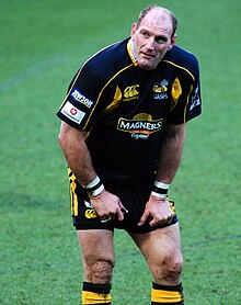 Photo en demi-grandeur d'un homme en maillot de rugby se tenant debout les mains appuyées sur les genoux