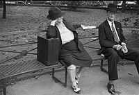 Scéna na Jackson Square, New Orleans, Louisiana, 1935; fotografie ženy a muže středního věku, sedící na lavičce v parku. Žena má neidentifikovaný kufřík, možná přenosnou Victrolu.