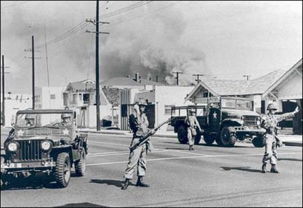 Soldiers of California's 40th Armored Division direct traffic away from an area of South Central Los Angeles burning during the Watts riot