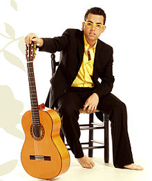 A man seated on a stool, with a guitar