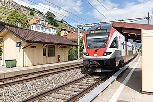 רכבת לבנה ואדומה על מסילה כפולה עם בניין חד קומתי משמאל