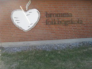 Bromma folkhögskola, skylt på fasaden, juni 2018. Folkhögskolans symbol äpplet kan ses som en symbol för kunskap.