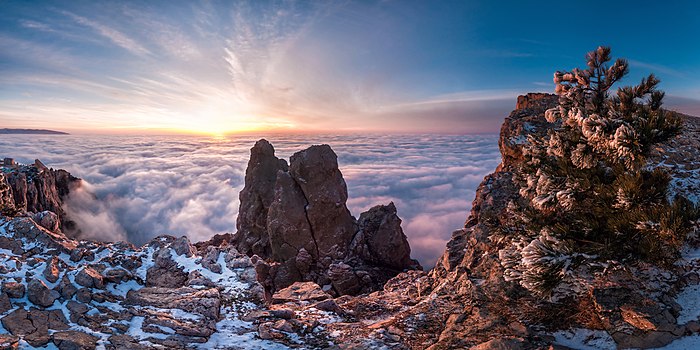 Несколько розовых камней, зубцов и присыпанных снегом, выступают из облака облаков под низким солнцем.