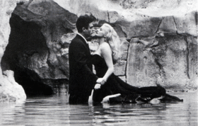 Un homme et une femme en tenue de soirée se font face, debout dans une fontaine