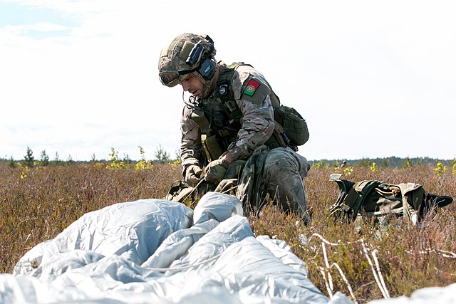 A Portuguese paratrooper gathers his chute and gear after landing into Adazi Base, Latvia, after conducting a high-altitude low-opening (HALO) jump