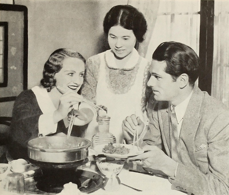 young woman and man seated at a table with maid standing centre