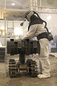 Person in protective gear working in the regolith bin of Swamp Works at NASA's Kennedy Space Center (Florida), testing the Regolith Advanced Surface Systems Operations Robot (RASSOR) Ksc-20190605-ph-kls02-0023.jpg