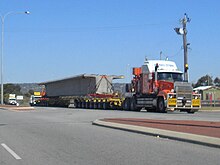 A truck with an oversize trailer carrying a concrete bridge beam