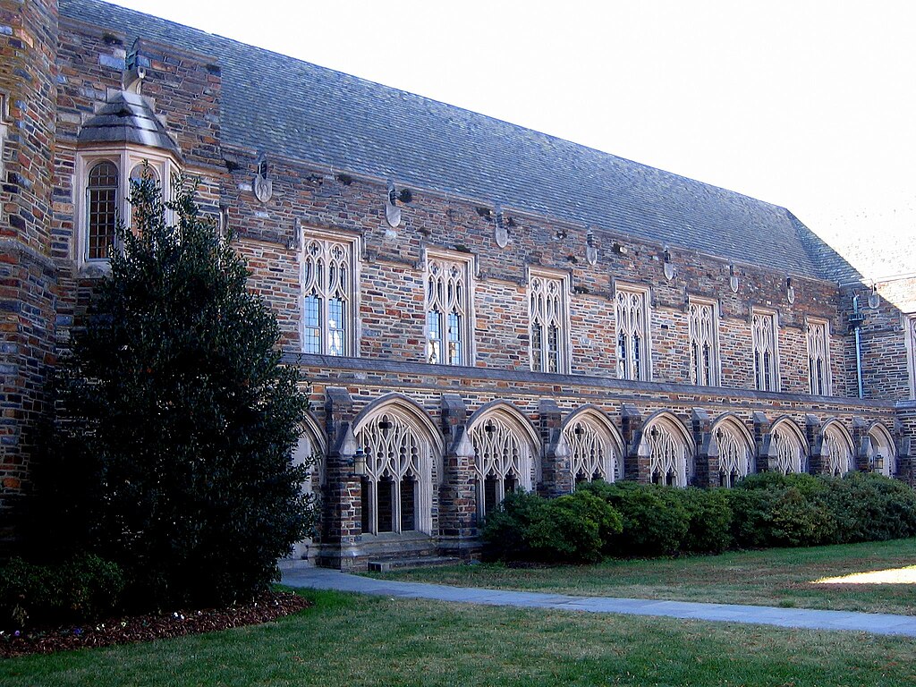 A Gothic-style exterior showcases Cathedral-like windows with the intricate framework and dark, colorful stone, with bushes and grass in the foreground