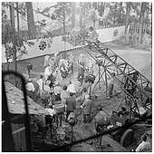 Photographie en noir et blanc prise en plongée lors du tournage du film, l'équipe technique est au premier plan et les acteurs au second plan.