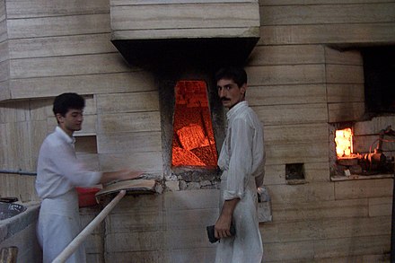 Two bakers baking sangak bread in a traditional oven