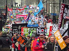 A large group of protestors holding various signs and flags. Many depict peace symbols and various anti-weopon sentiments.