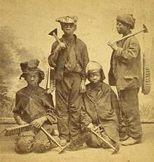 Un retrato de estudio de cuatro muchachos afroamericanos de Nueva York, con cepillos y raspadores, dos de pie y dos de rodillas.  Se ven entre los once y los catorce años, visten ropas toscas y sombreros y gorras maltratadas.