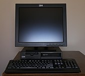 Musta pöytätietokone ja näyttö päällä sekä näppäimistö edessä.