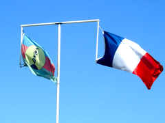 Two official flags of New Caledonia flying in Nouméa side by side from crossbar on flagpole.