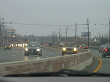 An eight-lane divded highway with a Jersey barrier that is lined with power lines and businesses