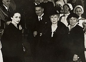 Photo of four people standing in the foreground, with nurses and others behind them