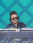 A dark-haired man performs on a set of turntables