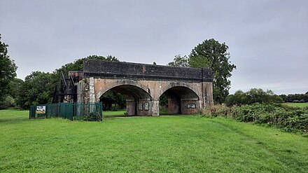 The former Somerset and Dorset Joint Railway bridge at Blandford Forum. Following closure of the line, the span over the river (right) was demolished, and the earth embankment on the left was reused for nearby flood defence work, leaving it as a "bridge to nowhere".