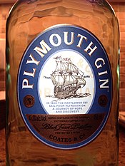 Close-up of bottle showing an oval label. Title "Plymouth Gin" in white capital letters placed curvilinearly around top edge of the oval, all in a wide blue band that borders the label. In the centre of the oval is a smaller white oval on which is a line drawing of a fully rigged sailing vessel. Below this in smaller blue type is: "In 1620 the Mayflower set sail from Plymouth on a journey of hope and discovery". The base of the oval has a gold-coloured section, with black type not clearly legible in the image, except that a company name "Coates & Co." in plain type can be seen, with "Black Friars distillery" in cursive script above that.