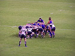 Fotografia de um scrum em uma partida da união de rúgbi, entre o time da Escócia com camisetas brancas e o time da Romênia com camisetas azuis