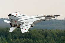 Photographie d'un MiG-25 en plein vol, au-dessus d'une forêt