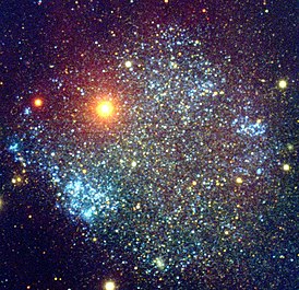 Неправильная галактика Секстант A. Яркие желтоватые звёзды Млечного пути на переднем плане. За ними лежат звезды Секстант A с молодыми синими звёздными скоплениями, хорошо видимыми.