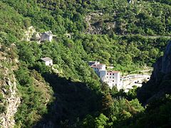 Photo couleur montrant une vallée montagneuse couverte de forêt. Dans la vallée, un bâtiment moderne haut de plusieurs étages.
