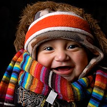 A baby wearing many items of winter clothing: headband, cap, fur-lined coat, scarf, and sweater Well-clothed baby.jpg