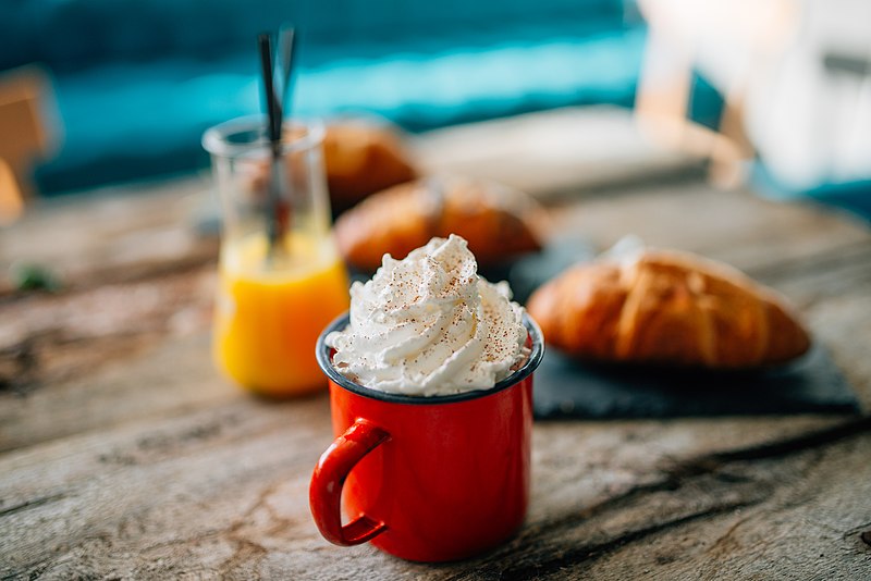 File:Cup of whipped cream with sprinkles with an orange juice glass and three croissants behind it displayed on a table (49430317643).jpg