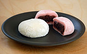 A plate with three ball-shaped rice cakes. One is white, two are pink; the pink ones are filled with a red paste.