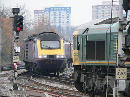 A Class 66 locomotive (right) is waiting at a red signal while a First Great Western passenger train (left) crosses its path at a junction.