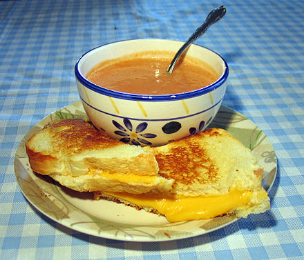 A grilled cheese sandwich made with American cheese served with a bowl of tomato soup