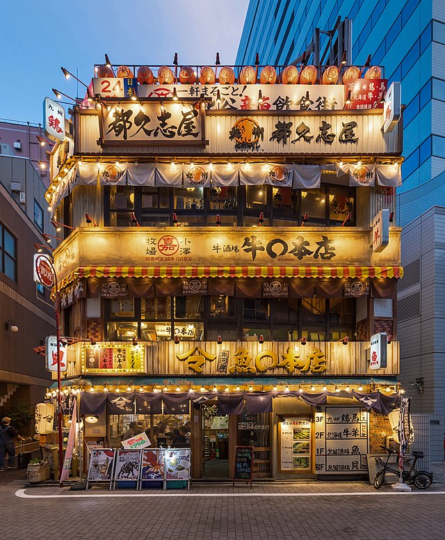 Освещённый фасад 3-этажного ресторана  с вывесками и красными бумажными фонарями в квартале Юраку токийского района Тиёда