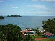 Vista a partir da costa de Kusapin, é possível ver algumas casas, vegetação e um corpo d’água