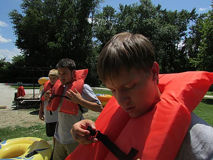 Lifejacket (model without rear part). To jump with it into the water, fasten the strap around the body and grab the front neck area with both hands.